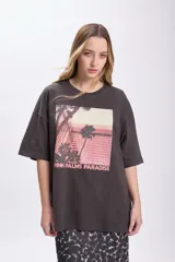 Remera de manga corta oversize color gris oscuro con estampa fotográfica de palmeras y edificio rosado.