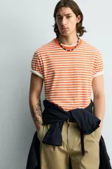 Camiseta de corte regular fit confeccionada en tejido de algodón, con diseño de rayas horizontales en color naranja y blanco, cuello redondo y manga corta.