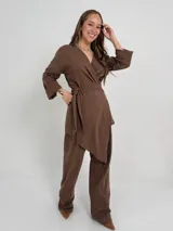 Conjunto de dos piezas confeccionado en lino color beige, compuesto por un pantalón de corte recto y un blazer cruzado con lazo ajustable en la cintura y escote en V.