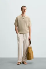 Polo de manga corta, color beige claro, con cuello solapa y cierre frontal de dos botones. Tejido de punto con textura acanalada vertical.