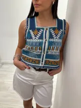 Chaleco corto en denim con bordado artesanal multicolor y escote cuadrado. Con cierre de botones y terminaciones desflecadas.
