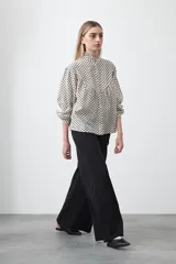 Camisa de viscosa con estampado de lunares, cuello alto con volados y cierre frontal de botones. Presenta un diseño de silueta suelta con frunces que aportan volumen y mangas largas con puños ajustados.