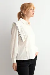 Camisa de color blanco con cuello clásico, cierre frontal de botones y mangas largas con puños. Presenta detalles de bordado geométrico en contraste a lo largo de los hombros y la parte superior de la espalda.