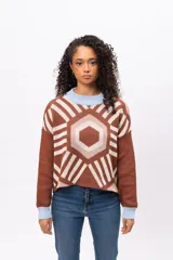 Buzo tejido de punto con diseño geométrico tipo mandala en tonos marrón, beige y blanco. Presenta cuello redondo y puños en color celeste pastel, con corte holgado y mangas largas.