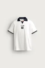 Polo de piqué de algodón color blanco, con cuello solapa azul marino y abertura frontal en V. Cuenta con mangas cortas con ribetes a rayas, y estampado frontal alusivo al Mundial USA 94.