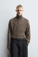 Jersey de punto de corte relajado, color marrón, con cuello perkins y cierre frontal de cremallera. Presenta manga larga y acabados en rib en puños y bajo.
