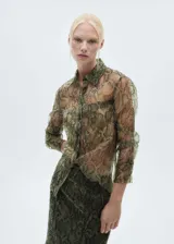 Camisa de organza semitransparente con estampado de serpiente en tonos marrones y verdes. Tiene corte recto, cuello camisero, dos bolsillos de parche en el frente y cierre de botones.