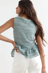 Blusa sin mangas de punto con textura arrugada, escote bote y diseño entallado con peplum y volados decorativos.