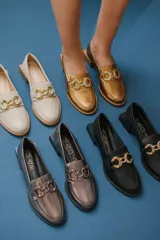 Mocasines de cuero en tono bronce metalizado, con detalle de aplique metálico dorado en el empeine y taco cuadrado bajo de madera.