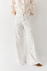 Pantalon de corte wide leg y tiro alto, color blanco con estampado de pequeños motivos deportivos coloridos. Cuenta con cierre frontal de botón y cremallera, y bolsillos laterales.
