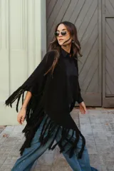 Poncho triangular tejido en lana, de color negro, con diseño inspirado en el poncho gaucho tradicional y terminaciones con flecos largos en los bordes.