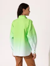 Camisa verde lima con degradé a blanco, de corte holgado, cuello mao con volantes y mangas largas con puños abotonados.