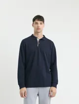 Remera de manga larga con cuello polo, confeccionada en tejido de punto canalé francés. Presenta abotonadura frontal con botones de madera y detalles a contratono en la cartera y el interior del cuello.