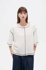 Remera de algodón color crudo, con cuello redondo a la base, mangas 3/4 holgadas y costuras con pespuntes en tono contrastante.