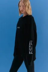 Sweater oversize de tejido de punto grueso en color negro, con cuello redondo y diseño de estampado gráfico en el pecho y en una de las mangas. Presenta un acabado desgastado que le otorga un estilo vintage.