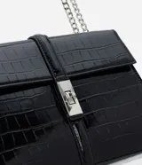 Cartera tipo shoulder bag de tamaño mediano, confeccionada en poliuretano con textura efecto croco. Presenta una tapa frontal con cierre metálico de giro, asa de mano reforzada y una correa larga de cadena plateada. Diseño estructurado con acabado sofisticado.