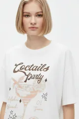 Remera blanca de algodón con cuello redondo, mangas cortas y calce holgado. Cuenta con un estampado frontal de estilo gráfico que dice "Negroni" junto con la ilustración de un trago y rodajas de naranja.