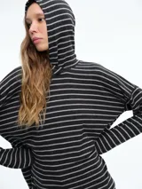 Buzo tejido de punto con diseño a rayas horizontales, corte holgado y capucha integrada. Presenta mangas largas con caída relajada y aberturas laterales en el ruedo.