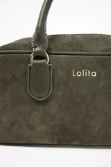 Cartera tipo satchel de diseño rectangular, confeccionada en gamuza color verde oliva. Cuenta con doble asa corta de mano, cierre superior con cremallera metálica y logo de la marca grabado en el frente.