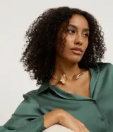 Gargantilla choker de metal con acabado en oro claro, con diseño rígido abierto que presenta un detalle de flor y pétalo texturizado en los extremos.