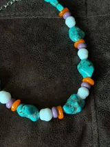 Collar corto compuesto por cuentas grandes de piedra turquesa irregular, alternadas con cuentas circulares blancas, naranjas y lilas.