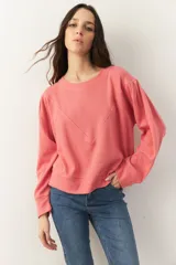 Buzo corto de manga larga con cuello redondo, confeccionado en tela texturizada. Presenta un diseño holgado con costuras decorativas en forma de V en el frente y puños ajustados.