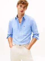 Camisa Tommy Hilfiger de corte regular en puro algodón Oxford, color celeste con sutiles rayas diplomáticas. Presenta cuello con botones, bolsillo de parche en el pecho con el logo bordado y mangas largas con puños redondeados.