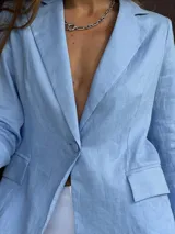 Blazer sastrero de lino en color celeste pastel, con cierre frontal de un botón forrado, solapas clásicas y bolsillos laterales con solapa. Presenta un corte estructurado y forro interior de algodón.