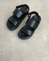 Sandalia negra de plataforma gruesa, con dos tiras anchas sobre el empeine y tira ajustable en el talón.