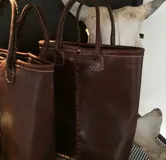 Matera de cuero vacuno en color marrón oscuro, con diseño artesanal de costuras visibles a la vista y doble manija superior.