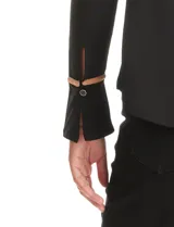 Blusa negra de crepe elastizado con ribetes en contraste color beige que recorren el escote en V, la línea central del frente y las costuras de los hombros. Tiene mangas largas con puños abiertos, abertura lateral y botón metálico.