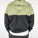 Campera deportiva combinada verde y negra de nylon, con capucha, cierre frontal y logo bordado en el pecho.
