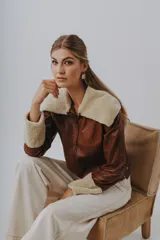 Chaqueta marrón de cuero Napa con cuello y puños de lana color crema, cierre frontal con cremallera y corte a la cintura.