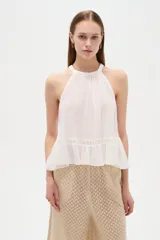 Top blanco de algodón con cuello halter, diseño holgado y detalle de encaje en el borde inferior.