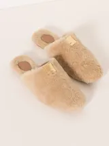 Pantuflas tipo slide color beige, confeccionadas en cuero de oveja con aplique metálico en el empeine, forrería de cuero caprino y suela de cuero vacuno.