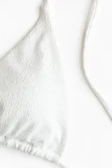 Top de bikini con textura fruncida, color blanco, de diseño triangular con tiras ajustables para atar en el cuello y la espalda.