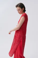 Kimono tejido de punto en color crudo con sutil brillo de lurex. Presenta un diseño sin mangas, corte largo y cierre frontal mediante dos lazos finos. El tejido tiene una textura acanalada vertical.