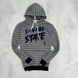 Canguro gris con rayas horizontales en tonos gris, rosa y blanco. Estampado frontal con la frase "Savage State" en letras negras. Tiene capucha con cordones blancos, bolsillo tipo canguro y puños negros.