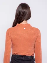 Top color beige de manga larga con cuello camisero y abertura ovalada en el escote. Su tela es flexible y consta de finas fibras metálicas.