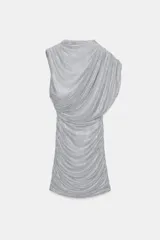 Vestido corto de tejido mesh plateado con aplicación de strass. Presenta cuello redondo, diseño sin mangas con drapeado en los hombros y una superposición efecto capa. Incluye frunces en los laterales y cierre oculto en el cuello.