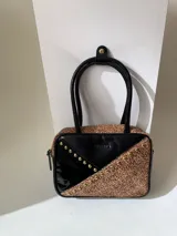 Cartera rígida negra con detalles en rojo y tachas plateadas. Tiene herrajes y cierre metálico plateado marca YKK, asa fina para llevar al hombro o en la mano y correa larga extra regulable. El interior es forrado, tiene un bolsillo con cierre enmarcado en cuero, y un segundo bolsillo plaqué.