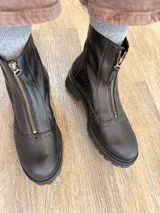 Botas de cuero negro con cierre frontal central y suela track. Presentan detalles de perforaciones tipo brogue en la puntera y laterales.