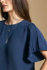 Top de color azul, con escote redondo a la base y mangas cortas amplias con caída fluida. Presenta una silueta relajada y un diseño minimalista.