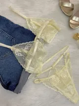 Conjunto de lencería de encaje color champagne, compuesto por un bralette estilo top con cierre frontal de gancho y una tanga de tiro alto con tiras regulables y diseño cut-out.