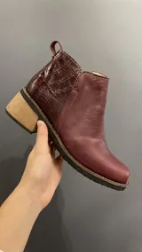 Botinetas de cuero vacuno color bordó, con diseño urbano y elegante. Presentan un detalle texturizado tipo cocodrilo en la parte trasera, taco bajo de madera y puntera cuadrada.