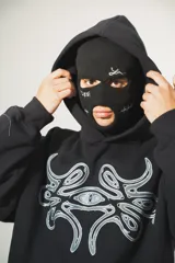 Hoodie negro oversize de algodón con capucha y pasamontañas desmontable con cierre. Presenta estampa en plastisol en el pecho y en ambas mangas.