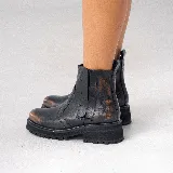 Bota corta estilo chelsea de cuero vacuno negro con acabado desgastado en tono marrón en la puntera y laterales. Presenta elástico lateral, cierre interno y suela de goma tipo track con plataforma.
