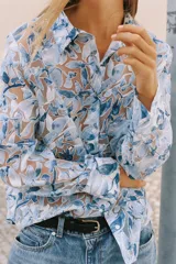 Camisa de manga larga con cuello solapa y cierre frontal de botones, confeccionada en tejido combinado semitransparente con estampado floral en tonos azules y blancos.
