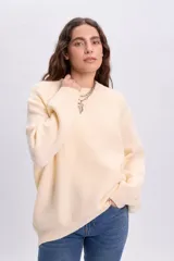 Buzo de punto color crudo, con cuello redondo y mangas largas, de diseño holgado y acabado clásico.