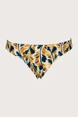 Calzón de bikini de corte a la cadera con cobertura pequeña. Presenta un estampado abstracto en tonos mostaza, negro y blanco, con un diseño que simula hojas o manchas. Es reversible, ofreciendo un segundo look.